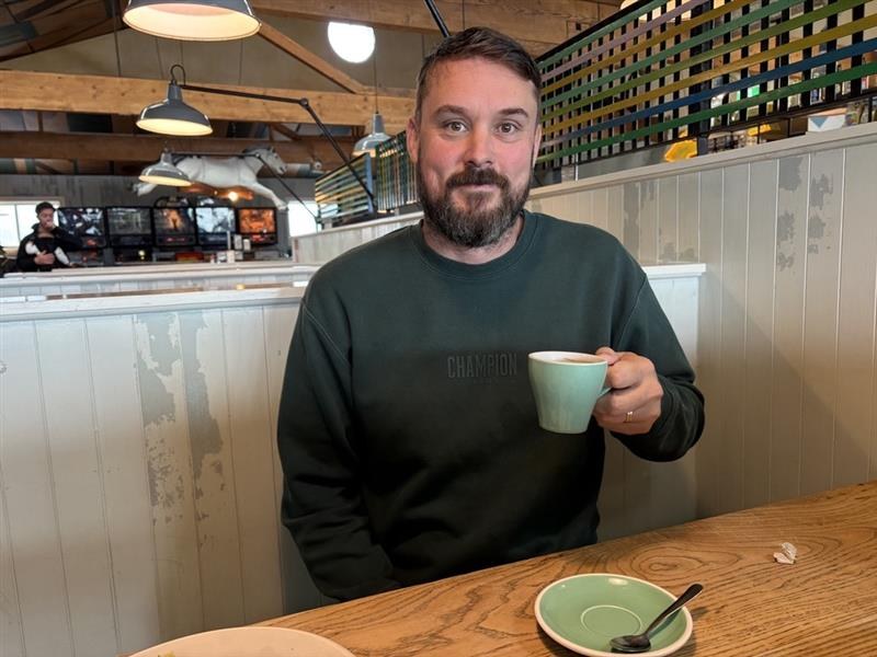 Samuel Hall holding a cup of coffee at a café